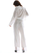 A model wears the white wide-leg pants in a back studio view showing the relaxed fit and lace hems.
