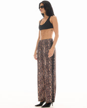 Three-quarter full-length view of the snake-print wide-leg pants styled with a black crop top, sunglasses and pointed heels against a white studio background.