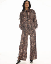 Full-length front view of the snake-print pants styled with the matching long-sleeve top and black pointed heels.