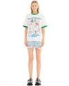 Full-length front view of a model wearing a white graphic T-shirt with green contrast trim, paired with light blue distressed denim shorts