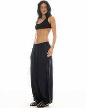 A model wears black wide-leg pinstripe pants with an elasticated waistband and embellished flat sandals in an angled front view.

