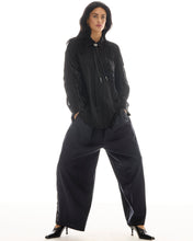 A model wears the black pinstripe tuxedo pants with a fringed black shirt and pointed heels in a full-length front view.
