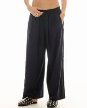 A close-up shows the elasticated waistband, side pockets and subtle pinstripes on the black wide-leg pants.
