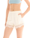 Close-up front view of the cream shorts showing the elastic waistband, side pocket and lace hem.