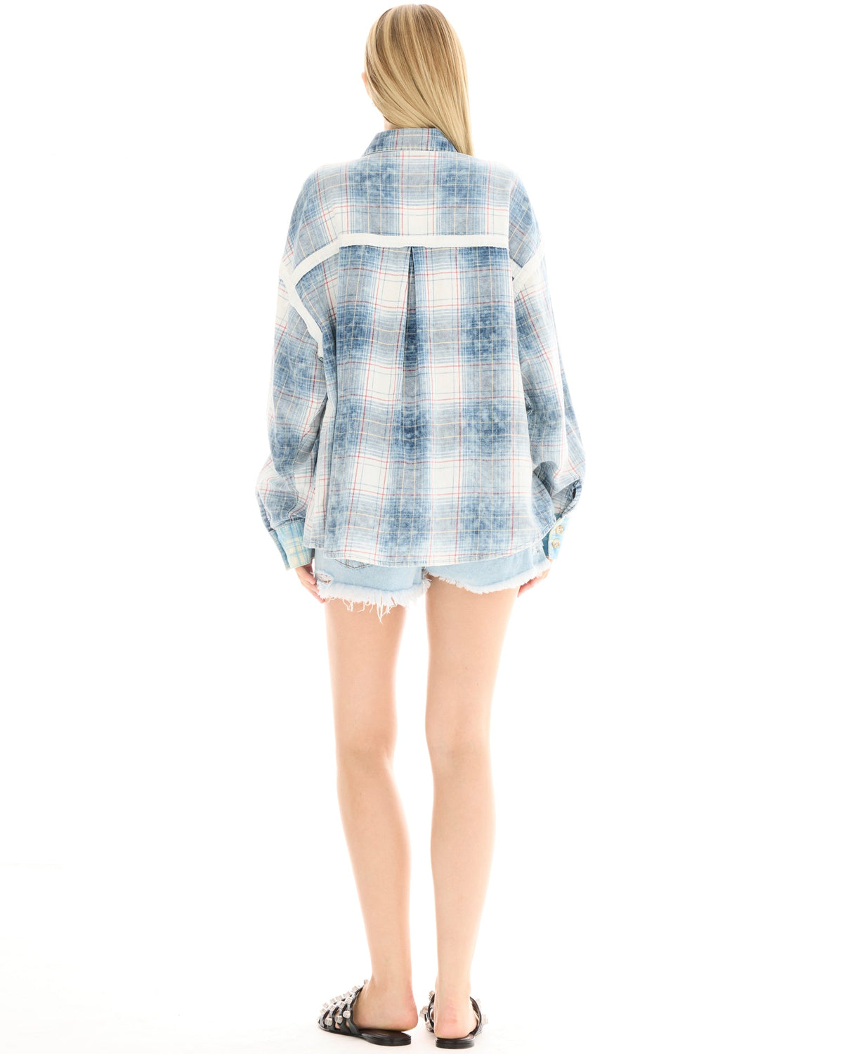 A woman wearing an oversized blue patchwork check shirt and denim shorts, shown from the back while standing with her arms relaxed at her sides.
