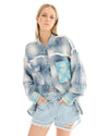 A woman wearing an oversized blue patchwork check shirt with denim shorts, standing facing the camera with her arms relaxed by her sides.