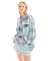 A woman wearing an oversized blue patchwork check shirt and denim shorts, standing at a three-quarter angle with one hand near her pocket.