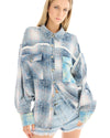 A woman wearing an oversized blue patchwork check shirt and denim shorts, standing at an angle while showing the relaxed shape of the shirt.