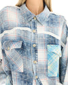 Close-up of a woman wearing a blue patchwork check shirt, showing the collar, button front, contrasting panels and western-style chest pockets.