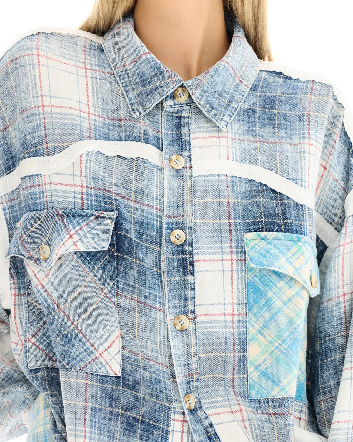Close-up of a woman wearing a blue patchwork check shirt, showing the collar, button front, contrasting panels and western-style chest pockets.
