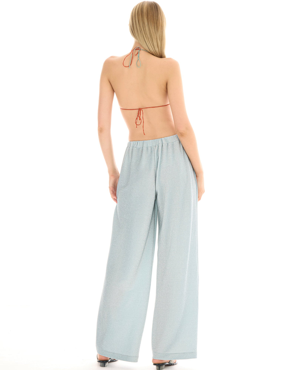 Back view of a woman wearing pale ice blue wide-leg lurex pants, showing the elasticated waistband and full-length loose silhouette.