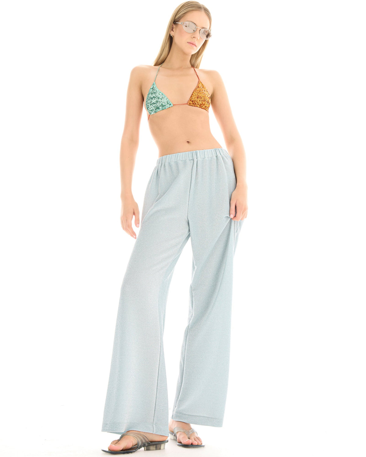 A woman wearing pale ice blue lurex pants in a relaxed front three-quarter pose, showing the wide-leg shape and subtle metallic shimmer.