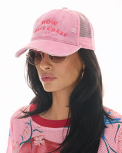 Close lifestyle view of the pink trucker cap worn with sunglasses and a colourful graphic mesh top against a bright studio background.