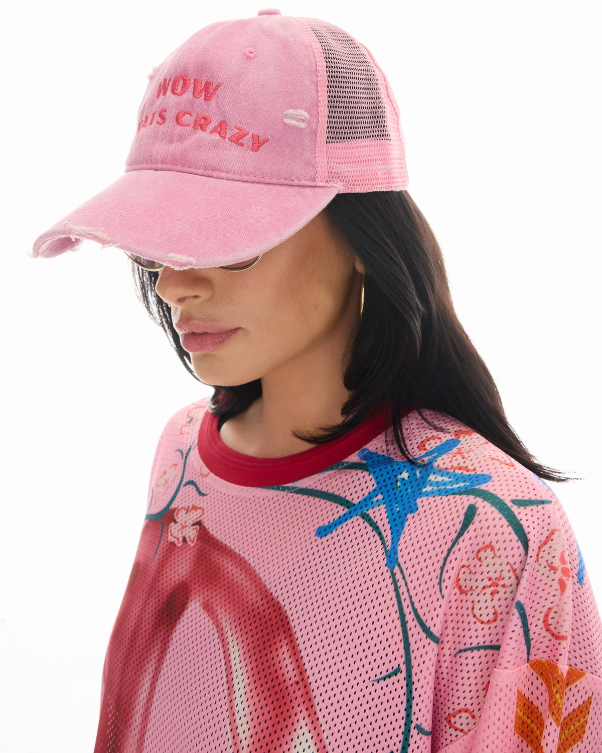 Side lifestyle view showing the distressed curved peak, embroidered slogan and pink mesh back while worn with sunglasses.